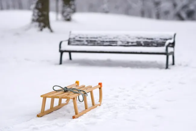Verschneiter Park mit Holzschlitten und Bank