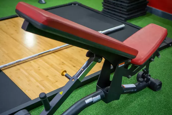 Verstellbare Hantelbank mit Langhantel und anderen Fitnesszubehör im Hintergrund in einem Fitnessstudio