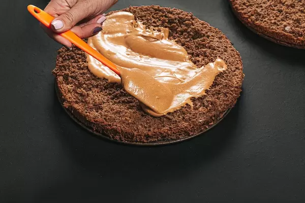 Verteilen der Creme auf einem Schokoladen Kuchen - Der Prozess der Zubereitung eines Kuchens