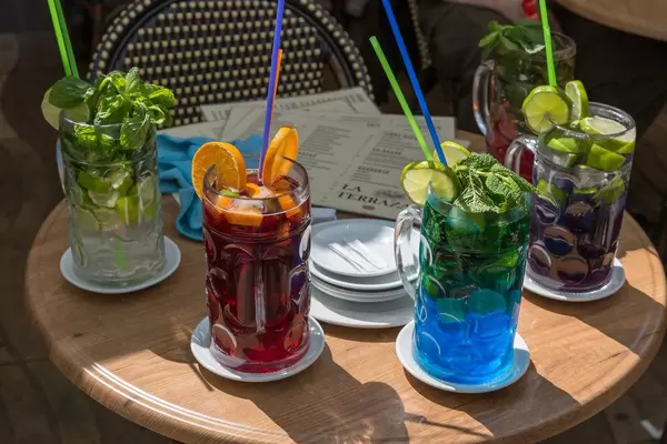 Vier bunte Cocktails in Biergläsern mit Limonenstücke, Orangenscheiben Minzblätter und Strohhalme im La Terraza Club in Barcelona, Spanien
