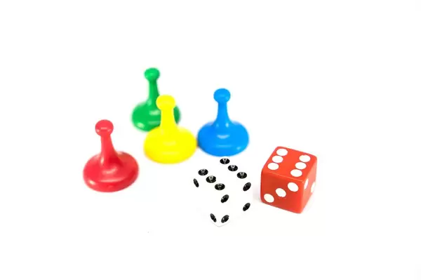 Vier farbige Spielfiguren mit rotem und weißem Würfel vor weißem Hintergrund