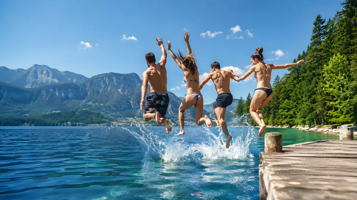 Vier Freunde springen vom Steg in einen Bergsee