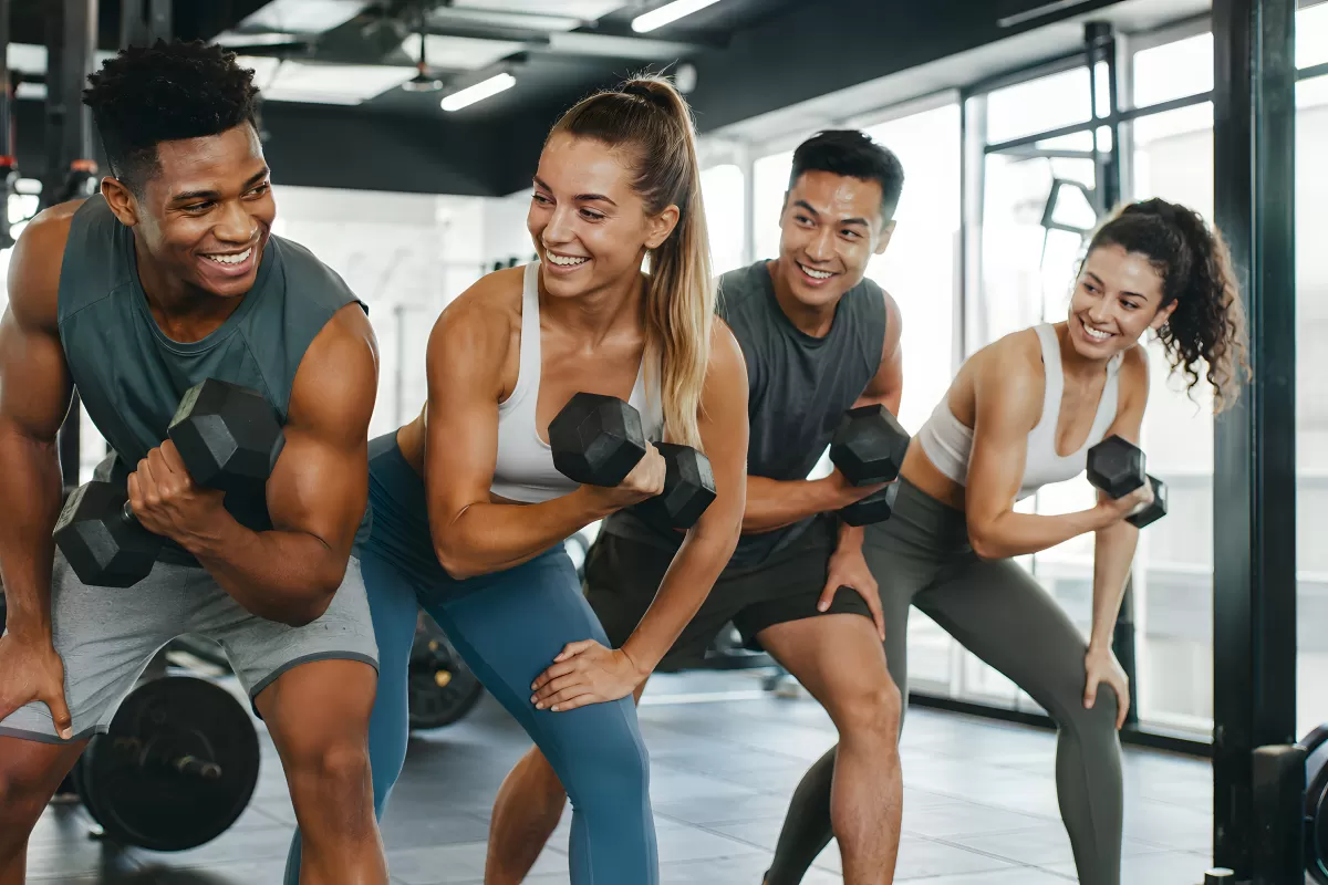 Vier Freunde trainieren gemeinsam mit Kurzhanteln im Fitnessstudio