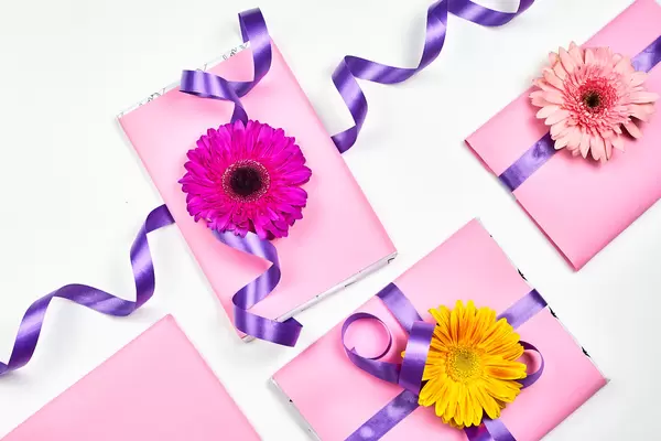 Vier Geschenke in Rosa verpackt und mit lila Schleife und bunten Blumen verziert. Weißer Hintergrund