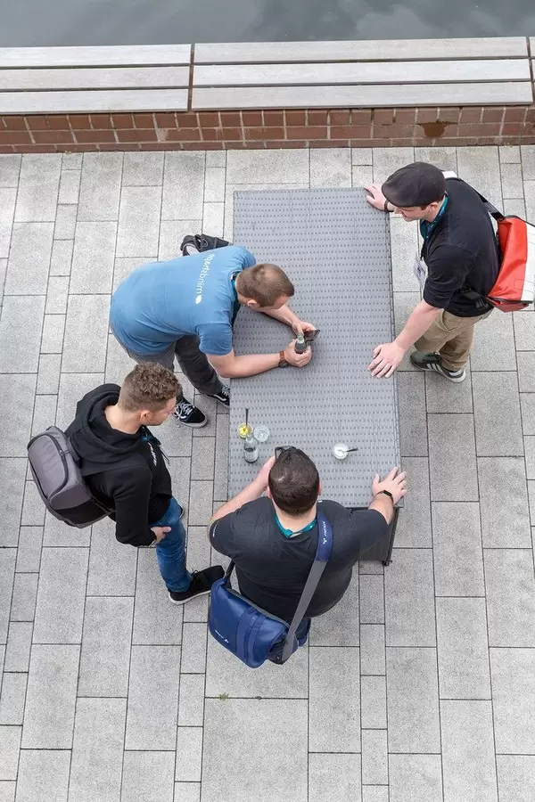 Vier junge Männer stehen an einem Rattantisch mit Handys und Getränken auf der Terrasse des AXA-Gebäudes beim Barcamp OMWest19 in Köln