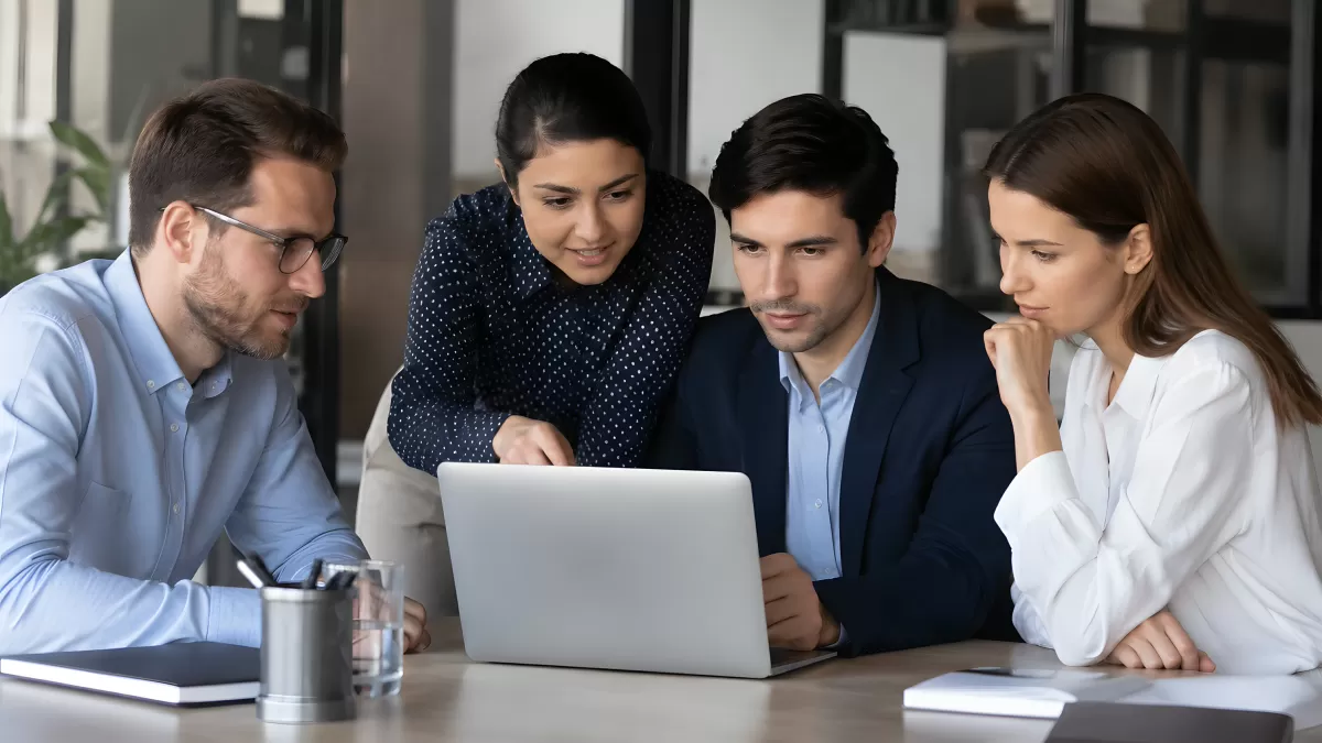Vier Kollegen analysieren gemeinsam Laptop-Bildschirm
