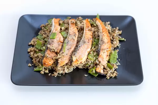Vier Lachssteifen gegrillt auf Blumenkohl-Quinova verfeinert mit Parmesankäse vor weißem Hintergrund