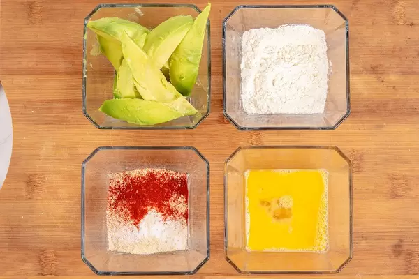 Vier Schüssel mit geschnittener Avocado, Mehl, Ei und Paniermehl mit Paprikapulver