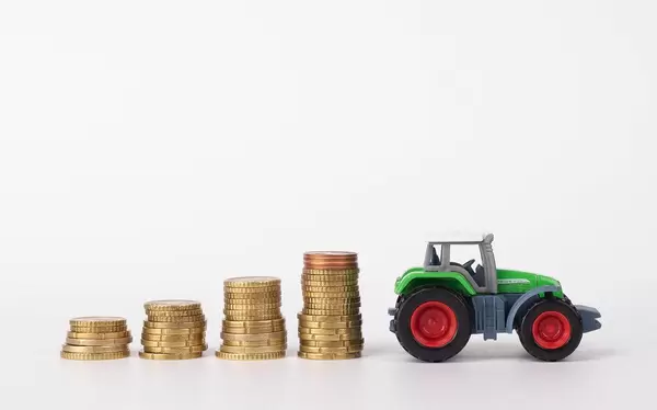 Vier Stapeln Euromünzen und ein Spielzeugtraktor vor weißem Hintergrund