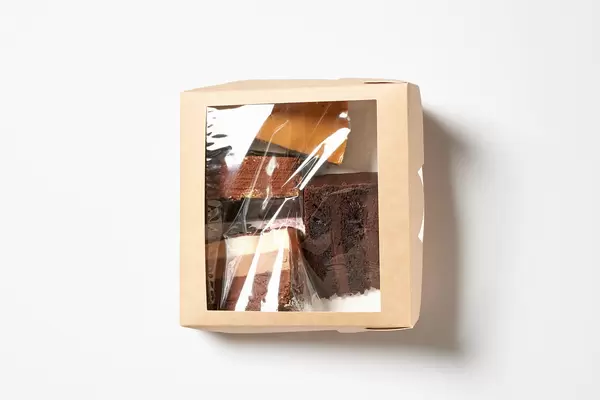 Vier verschiedene Tortenstücke in transparenter Verpackung-Box vor weißem Hintergrund