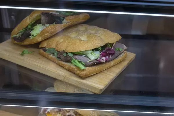 Viereckige Brötchen mit Salat und dunklem Schinken belegt, auf einer Glastheke in einem Café in Barcelona, Spanien