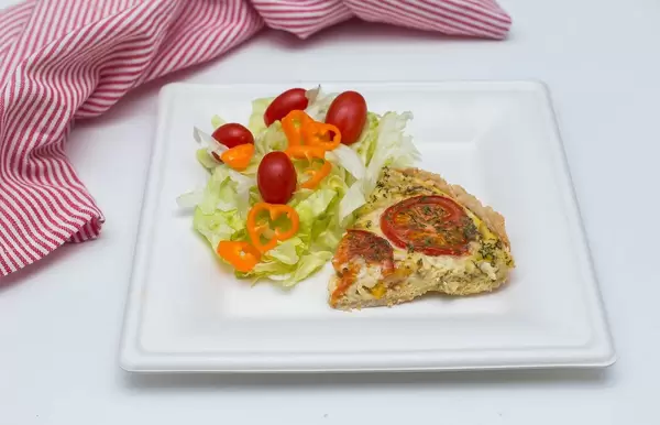 Viertel Quiche mit Gemüse und Kräutern mit Salat, Tomaten und Paprika auf weißem Teller