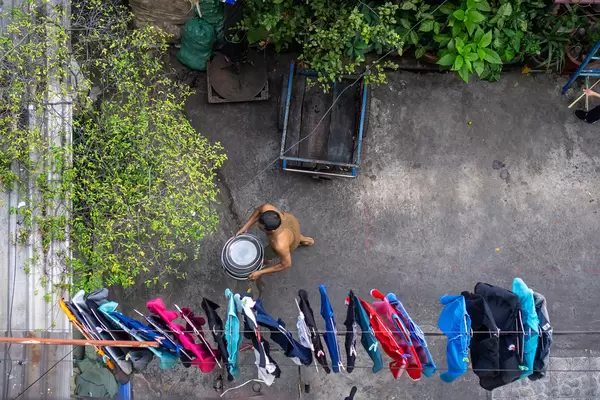 Vietnamese Man carrying Large Bowls inside an Alley with Laundry hanging on a Clothes Line in a Local Area in Saigon, Vietnam