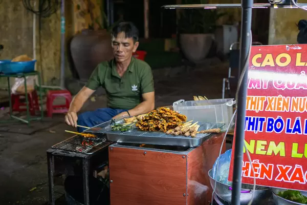 Vietnamese Man grilling Pork, Beef and Chicken Skewers on a Barbecue Grill at a Street Food Restaurant in Hoi An, Vietnam