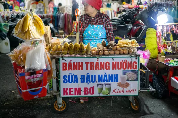 Vietnamese Woman selling Grilled Rice Paper Snack, Hot Soy Milk, Avocado Ice Cream and other Snacks from a Street Food Cart at the Dalat Night Market