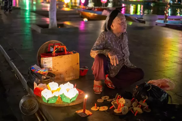 Vietnamese Women sitting on the Sidewalk selling Floating Paper Lanterns with Candles at Night to release in Thu Bon River in Hoi An, Vietnam