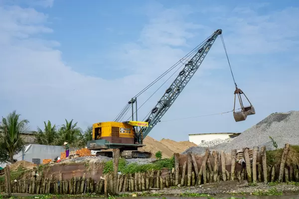 Vietnamese Worker next to a Excavator Crane on a Building Construction Site with Pebbles and Sand in Can Tho, Vietnam