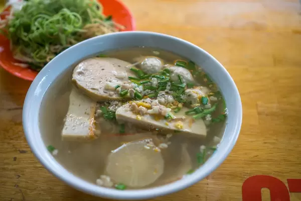 Vietnamesische Nudelsuppe mit Klößen und Kräutern im Hintergrund