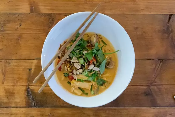 Vietnamesisches Mittagessen mit Essstäbchen: Veganes Bio-Tofu in roter Kokoscurry-Sauce mit Cherrytomaten, Babyauberginen & Erdnüssen
