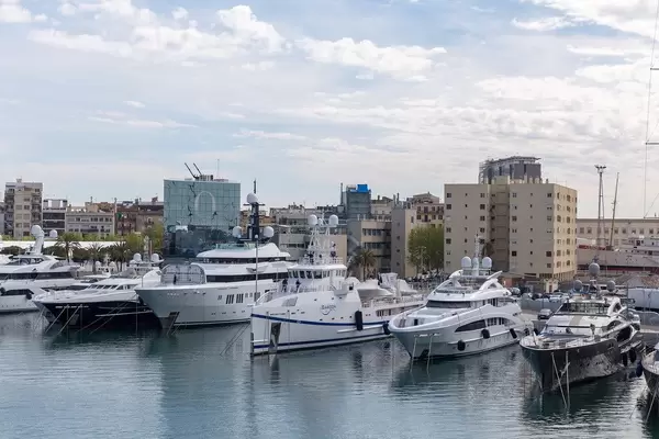 View from tourist attraction and bridge Rambla de Mar to yachts and luxury boats in Port Vell harbour with tower clock in Barcelona, Spain