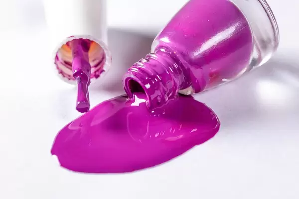 Violetter Nagellack mit Flasche und Pinsel ausgeschüttet auf weißem Hintergrund