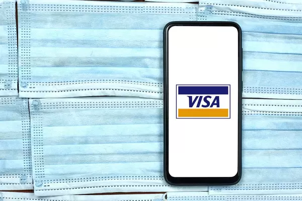 Visa company logo on smartphone screen over the face masks. Global company during coronavirus crisis