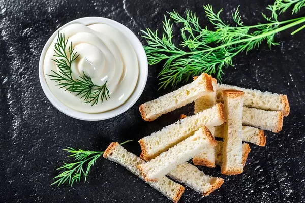 Vogelperspektive von Weißbrot-Cracker, weißer Sauce und Dill auf schwarzem Untergrund