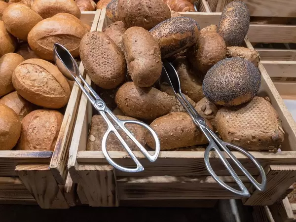 Vollkornbrötchen mit Mohn in Körben mit Zangen zum Servieren an einem Frühstücksbuffet
