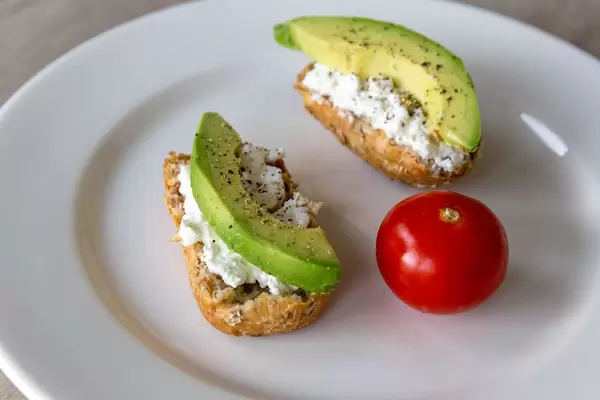 Vollkornbrote belegt mit Hüttenkäse und Avocadoscheibe mit Pfeffer und ganzer Tomate