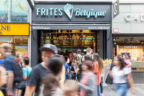 Vorbeilaufende Passanten und das Frites Belgique Fastfoodlokal im Hintergrund