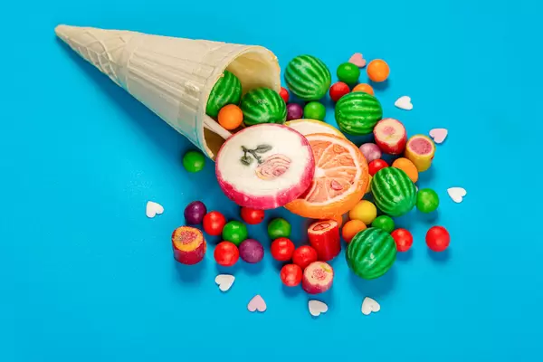 Wafer cone and scattered candies with lollipops on blue background