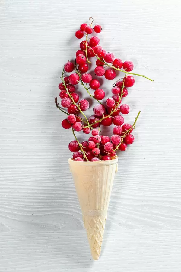 Waffle cone filled with red currant berries on white wooden background (Flip 2019)