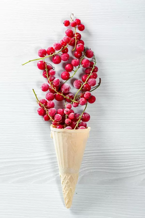 Waffle cone filled with red currant berries on white wooden background
