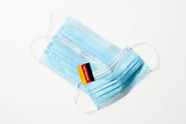 Wahl 2021: drei OP-Masken vor weißem Hintergrund und eine deutsche Flagge mit Schrift "Abstimmung"