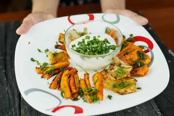 Waitress putting a plate of healthy vegetable chips with delicious dipping sauce on the table