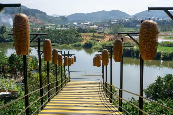 Walkway Bridge with Hanging Lanterns leading to a View of a Lake and Mountains at Me Linh Coffee Garden in Da Lat, Vietnam