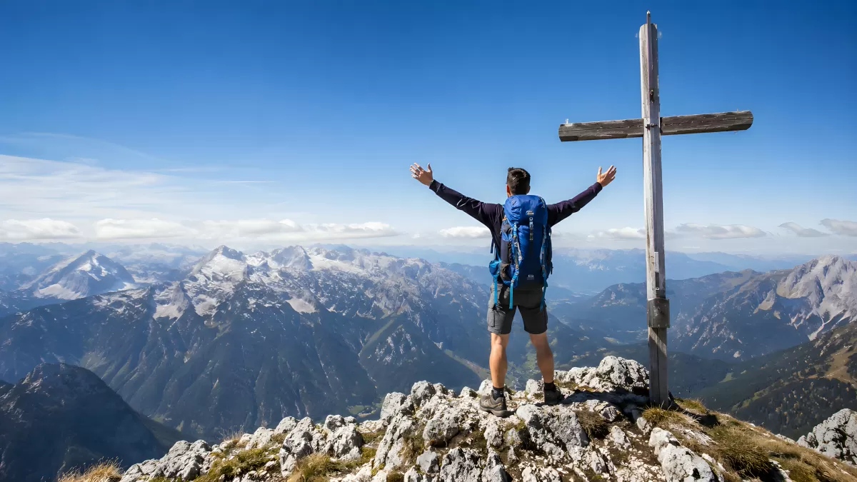 Wanderer auf Berggipfel mit Holzkreuz und Alpenpanorama — Bild kostenlos herunterladen