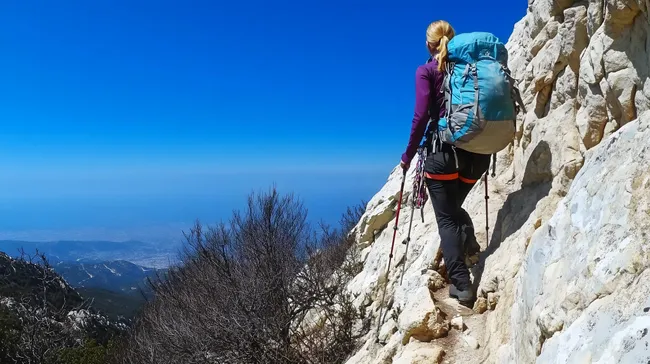 Wanderer mit Rucksack auf felsigem Berg bei blauem Himmel