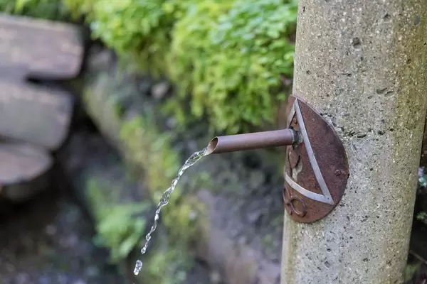 Wasser fließt aus einem Trinkbrunnen aus Stein und Metall im Grünen an dem Mühlbachweg in Alpbach