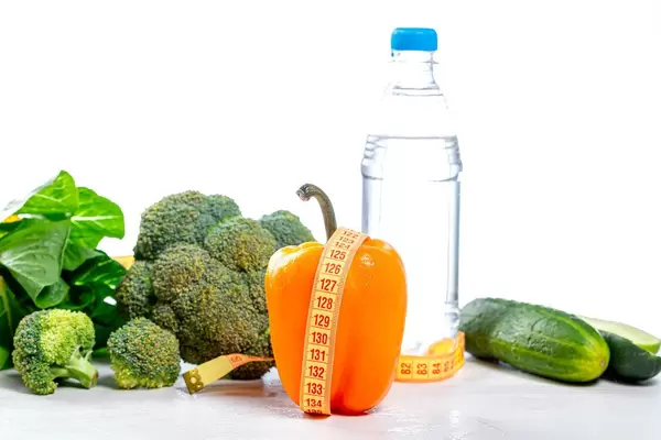 Wasserflasche und frisches Gemüse vor weißem Hintergrund mit Maßband - Konzept der Ernährung und Gesundheit - Lifestyle