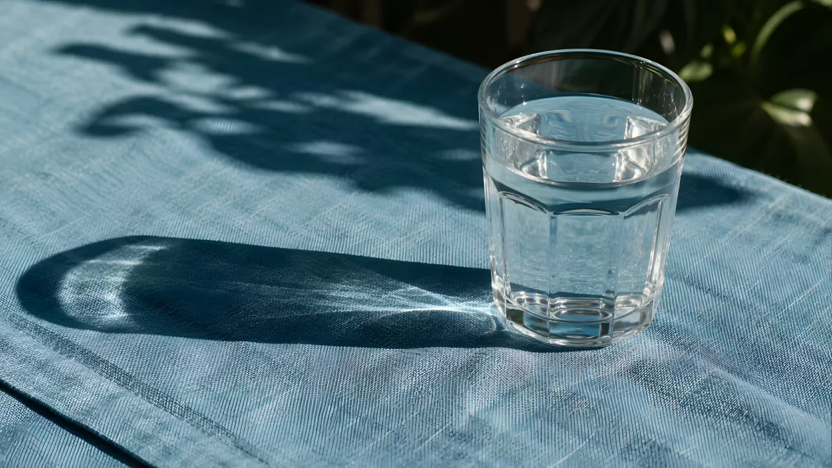 Wasserglas im Sonnenlicht auf blauem Leinentuch
