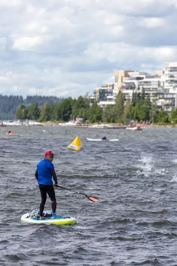Water sportsman on a stand-up paddleboard at the edge of the swimming contest for the Finnish Ironman 70.3, observing triathletes in the lake