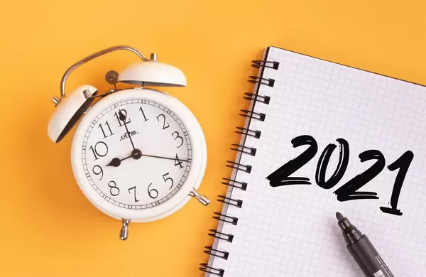Wecker und ein Heft mit ‘2021’ Text mit einem Filzstift drauf vor gelbem Hintergrund