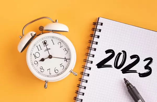 Wecker und ein Heft mit ‘2023’ Text mit einem Filzstift drauf vor gelbem Hintergrund