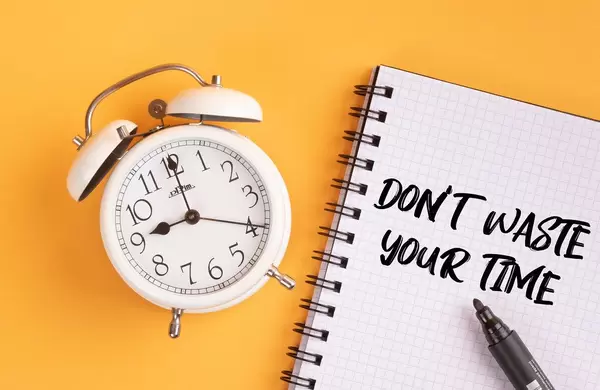 Wecker und ein Heft mit ‘Don’t waste your time’ Text mit einem Filzstift drauf vor gelbem Hintergrund