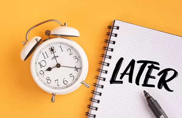 Wecker und ein Heft mit ‘Later’ Text mit einem Filzstift drauf vor gelbem Hintergrund