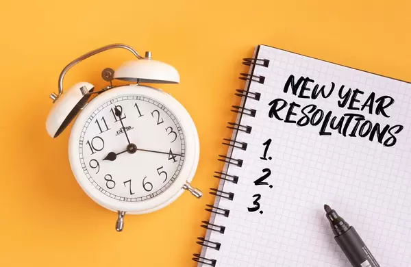 Wecker und ein Heft mit ‘New year resolutions’ Text mit einem Filzstift drauf vor gelbem Hintergrund