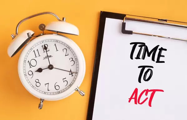 Wecker und ein Klemmbrett mit dem handgeschriebenen Text "time to act / Zeit zu Handeln", vor gelbem Hintergrund