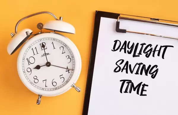 Wecker und ein Klemmbrett mit dem Text "Daylight Saving Time / Sommerzeit", vor gelbem Hintergrund