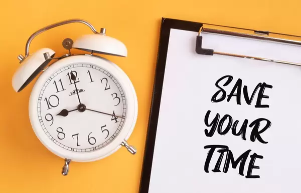 Wecker und ein Klemmbrett mit dem Text "Save your time / Zeit sparen", vor gelbem Hintergrund